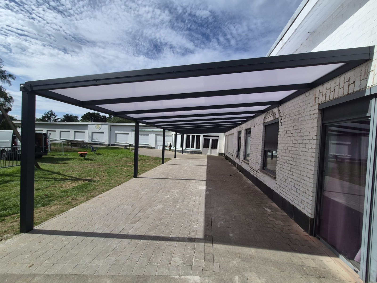 Schooloverkapping met plat dak tegen de gevel, aluminium structuur en polycarbonaat dakbedekking