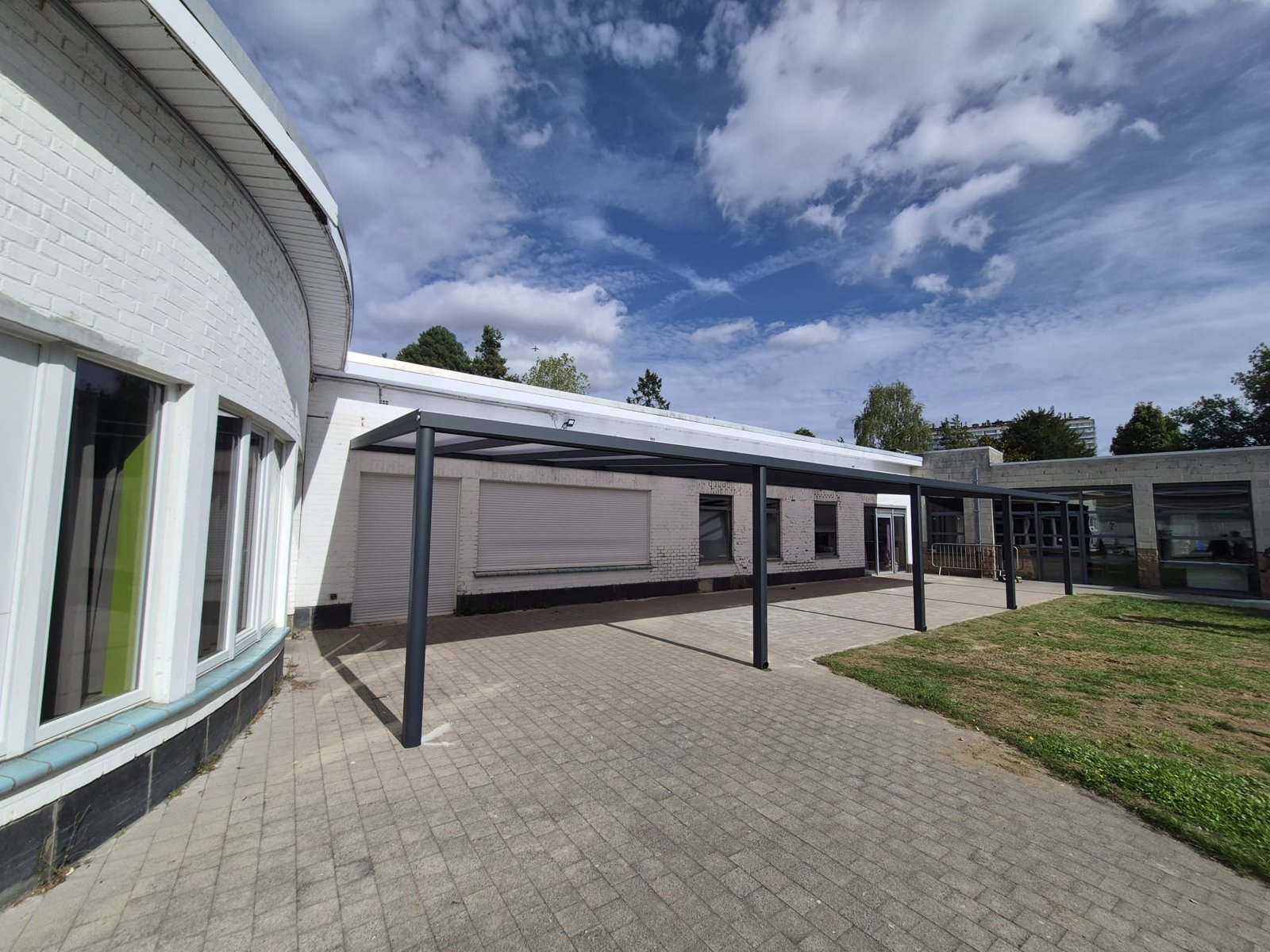 Overkapping met plat dak die de gebogen gevel van een schoolgebouw volgt